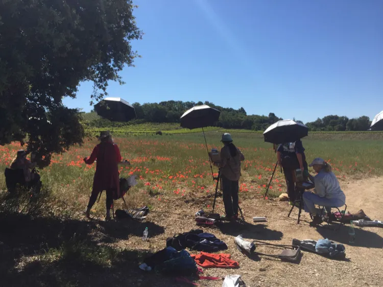 A group of painters working beneath umbrellas beside a poppy field